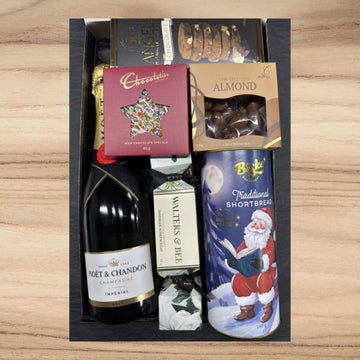 Gift basket with Moet & Chandon champagne, shortbread, and other items on a wooden surface
