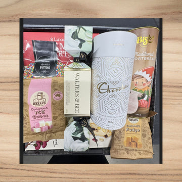 Gift box with various items including a tumbler, snacks, and a bottle on a wooden surface.