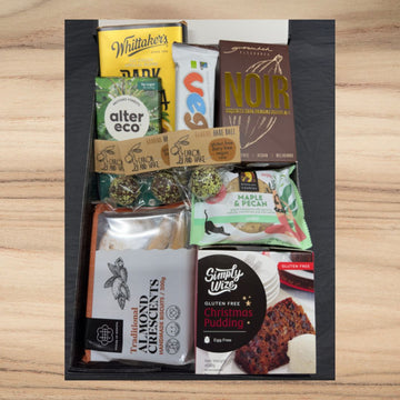 Assorted gluten-free snacks including dark chocolate, cookies, almond biscuits, and Christmas pudding in a gift box
