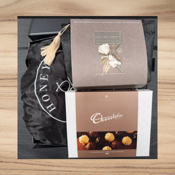 Gift hamper with Classic White Florals bath set and Chocolatier milk and dark truffles on wooden surface