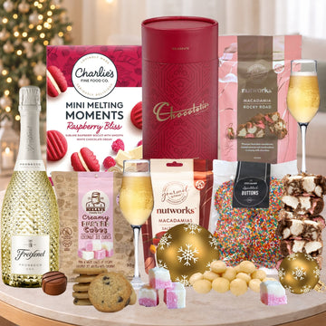 Assorted gourmet food items including a bottle of Freixenet, chocolate, and cookies on a table with a festive background.