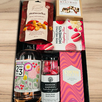 Assorted gourmet items including a bottle of vodka, candies, and cookies on a wooden surface.