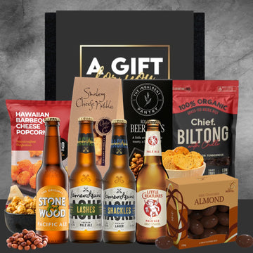 Gift set with beer bottles, snacks, and a 'Chief Biltong' package on a gray background.