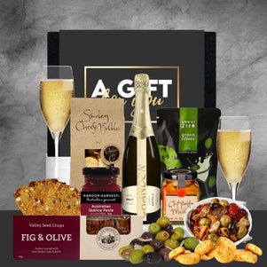 Gourmet gift basket with champagne, snacks, and assorted foods on a gray background