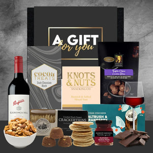 Collection of gourmet snacks, wine, and coffee on a gray background with 'A Gift for You' box.