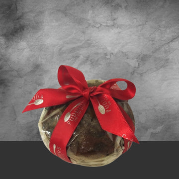 Festive Christmas pudding cake wrapped in cello with a red ribbon bow on gray background