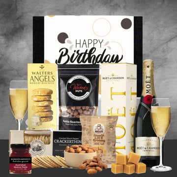 Birthday gift basket with snacks, chocolate, and champagne on a gray background