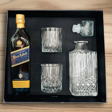 Johnnie Walker Blue Label bottle with glasses and a decanter set in a box on a wooden surface