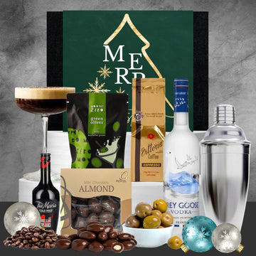 Gourmet gift set with drinks, snacks, and cocktail accessories on a gray background.