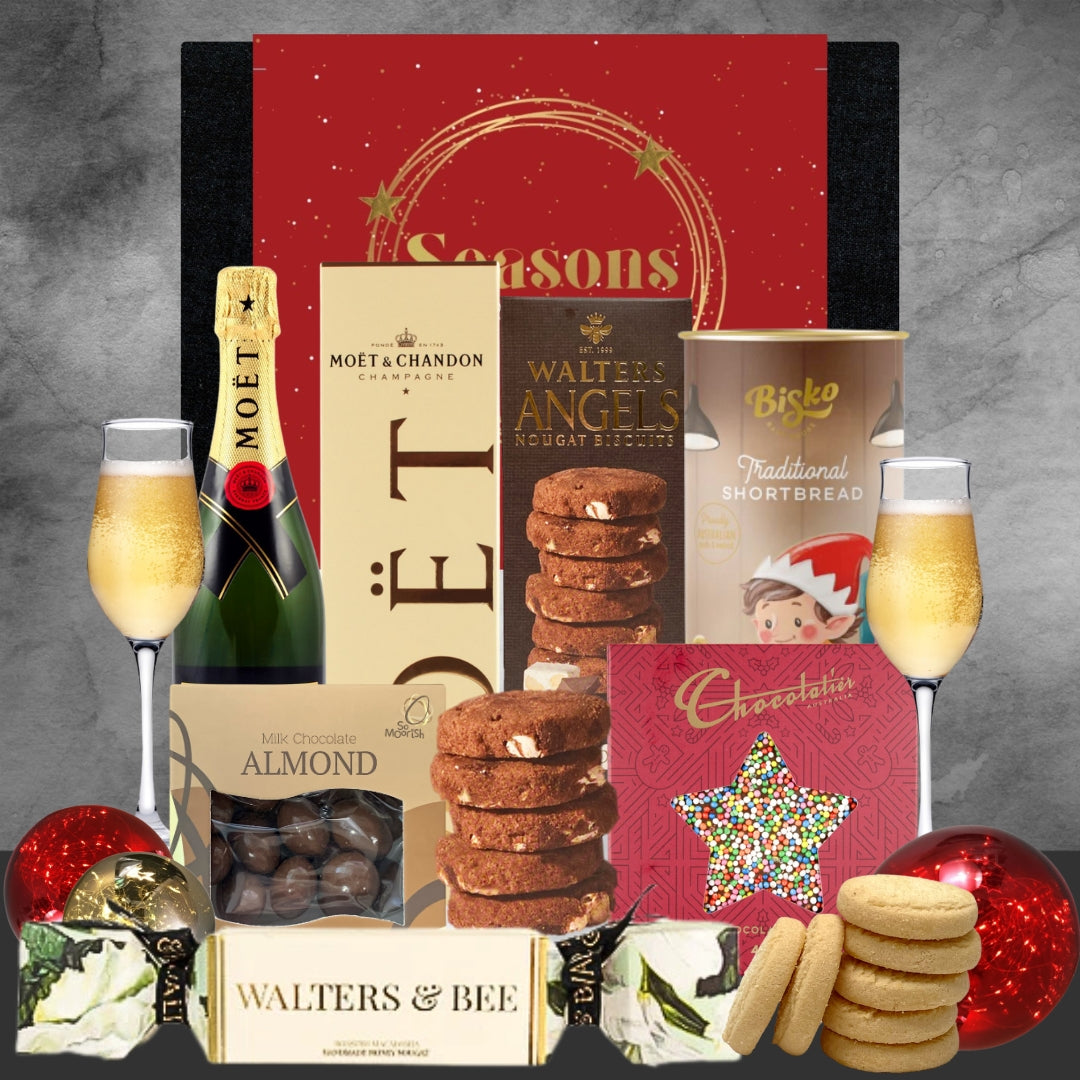 Gourmet gift set with champagne, cookies, and other treats on a gray background