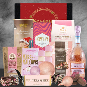 Assorted holiday treats including marshmallows, shortbread, and a bottle of rose wine on a gray background.