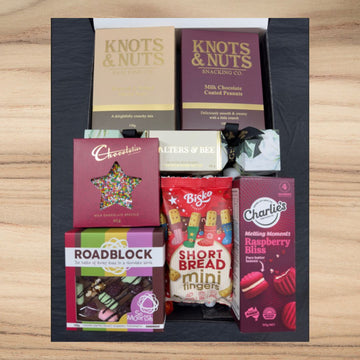 Gift box with assorted snacks including Knots & Nuts nuts, Chocolatier chocolate, Alters & Bee chocolate, Roadblock rocky road, Bisko shortbread, and Charlie's raspberry bliss