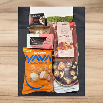 Assorted snack pack including YAVA sea salt caramel popcorn, Nutworks salted chili macadamias, vegan rocky road bar, and other gourmet treats