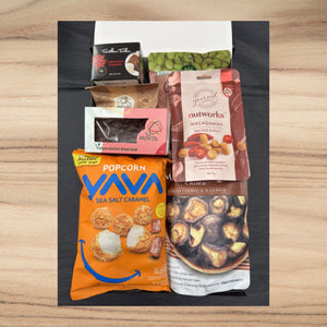 Assorted snack pack including YAVA sea salt caramel popcorn, Nutworks salted chili macadamias, vegan rocky road bar, and other gourmet treats