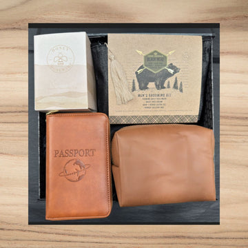 Men's gift set with tan leather passport cover, grooming kit with black bear design, beige toiletry bag, and natural coffee cup