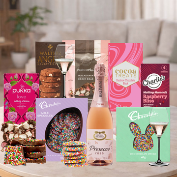 Assorted gift items including chocolate, cookies, and a bottle of Prosecco on a table.