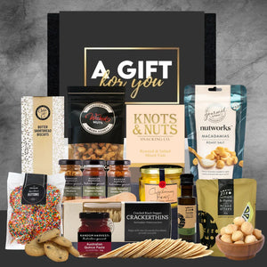 Assorted gourmet food items arranged in front of a 'A Gift for You' box on a gray background.