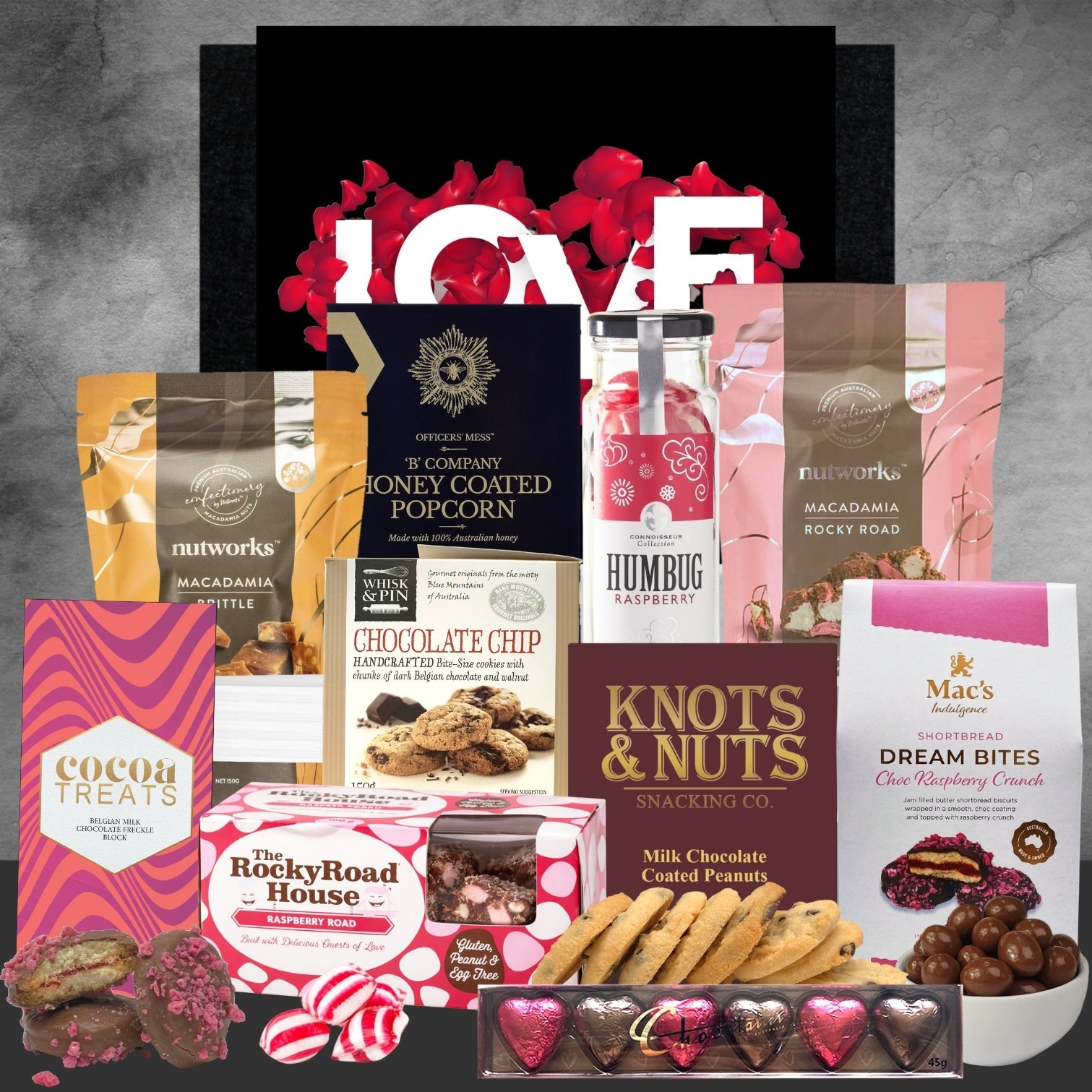 Assorted gourmet snacks and candies with a 'LOVE' sign in the center on a gray background.