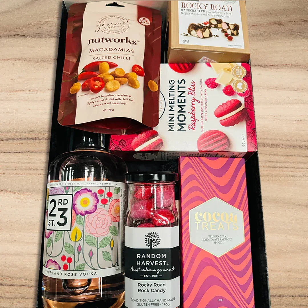 Assorted gourmet items including a bottle of vodka, candies, and cookies on a wooden surface.