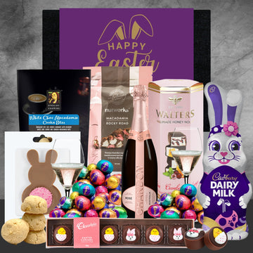 Easter gift basket with chocolate eggs, cookies, and a bottle of champagne on a gray background.