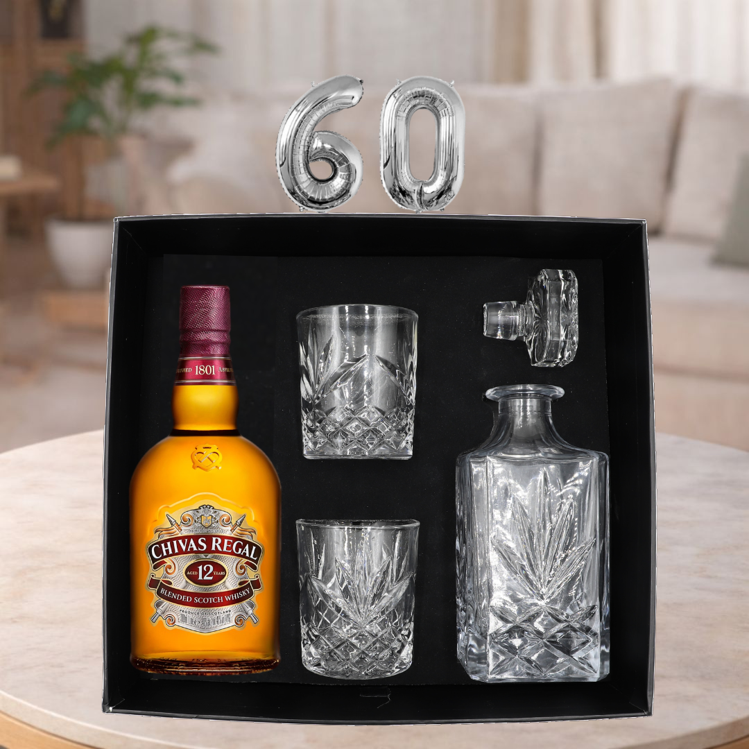 Chivas Regal 12 whisky bottle with glasses and decanter set in a black box, with '60' on top, on a table.
