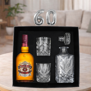 Chivas Regal 12 whisky bottle with glasses and decanter set in a black box, with '60' on top, on a table.