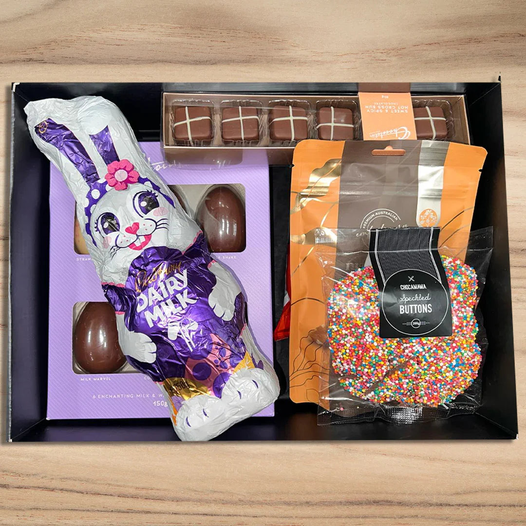 Chocolate Easter bunny, chocolate eggs, and a bag of colorful buttons in a black box on a wooden surface.