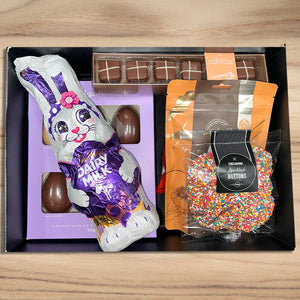 Chocolate Easter bunny, chocolate eggs, and a bag of colorful buttons in a black box on a wooden surface.