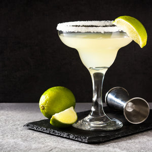 Cocktail in a martini glass with a salt rim and lime wedge, served on a dark surface.