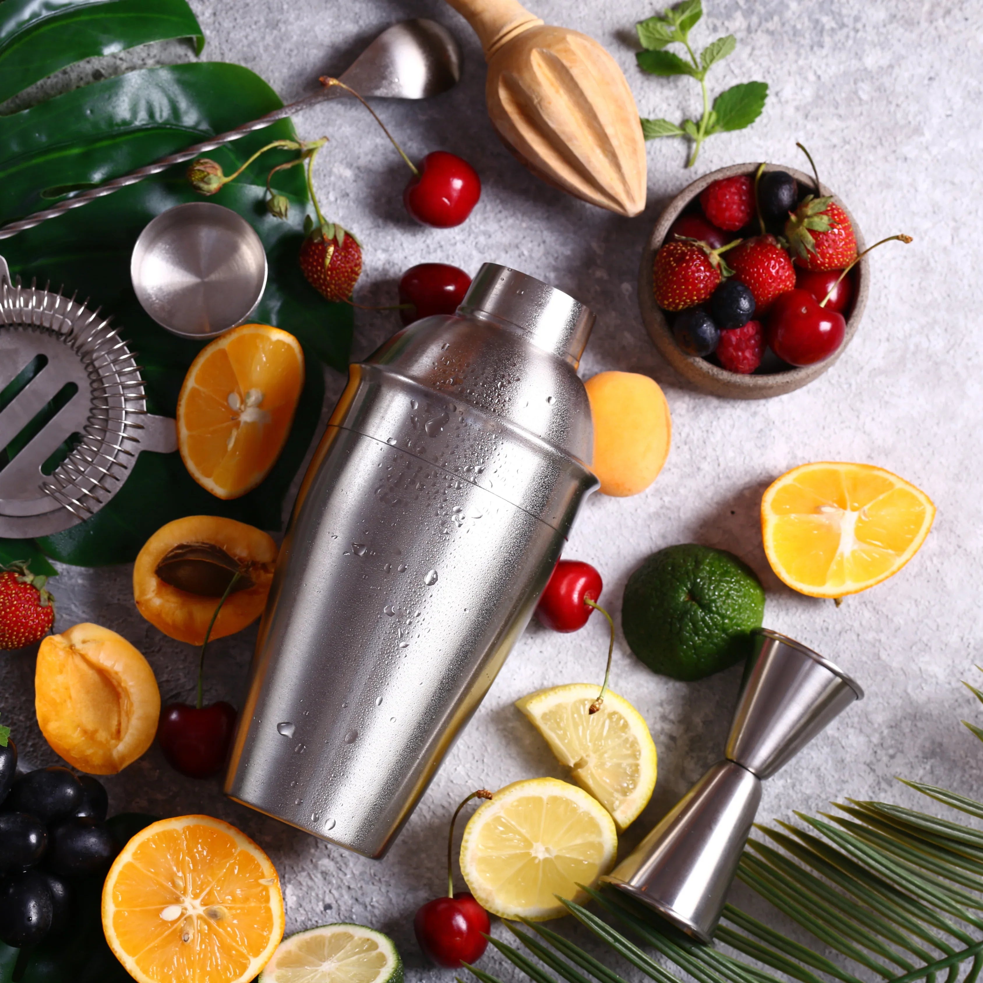 Cocktail shaker with fruits and bar tools on a textured surface