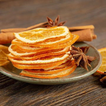 Stack of dried orange slices on a plate with cinnamon sticks and star anise on a wooden surface