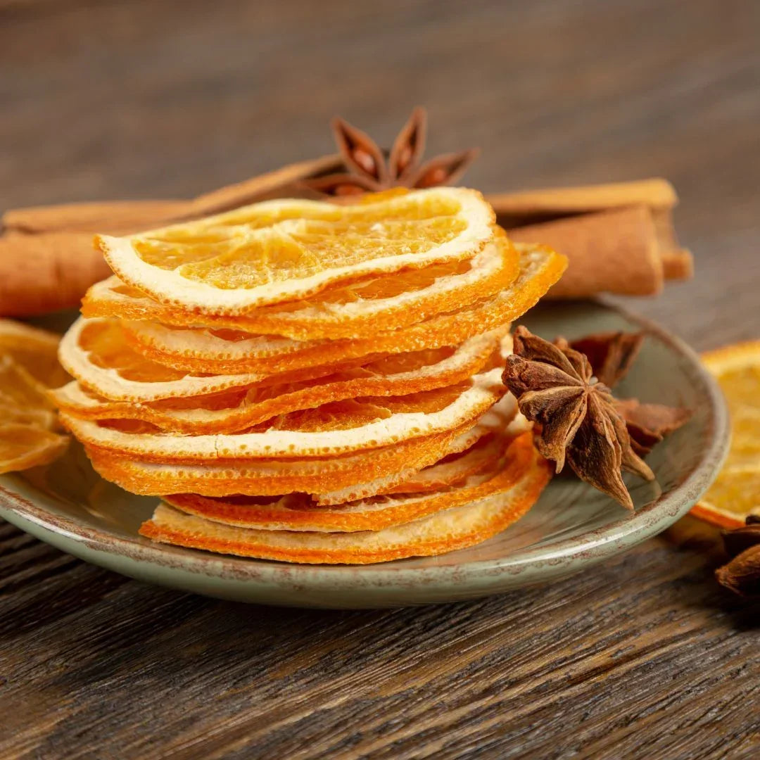 Stack of dried orange slices on a plate with cinnamon sticks and star anise on a wooden surface