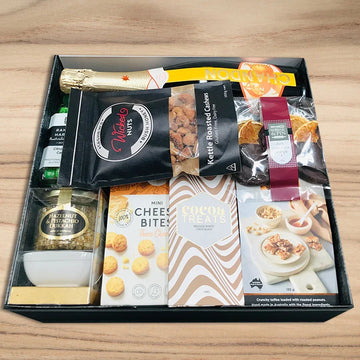 Gift box with snacks, drinks, and a bottle on a wooden surface