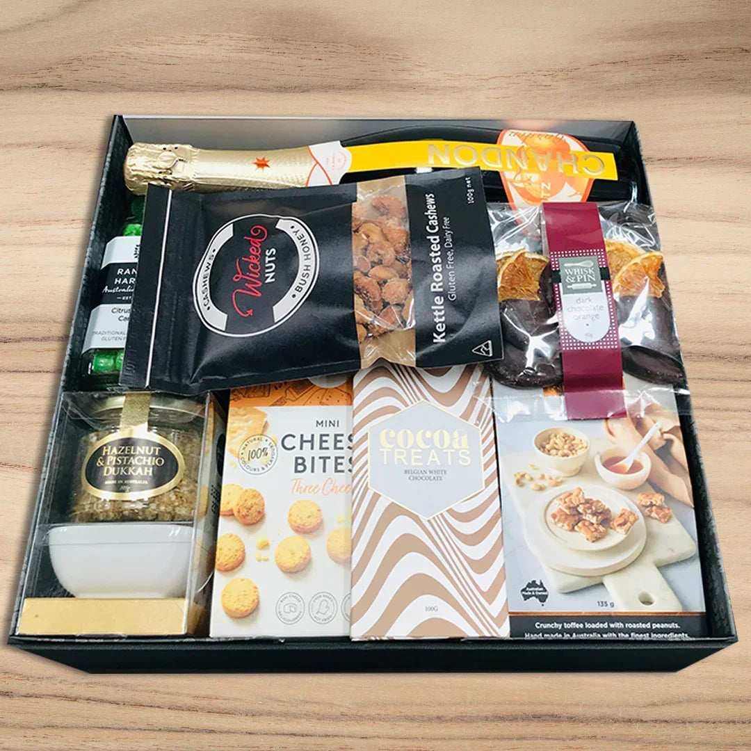 Gift box with snacks, drinks, and a bottle on a wooden surface