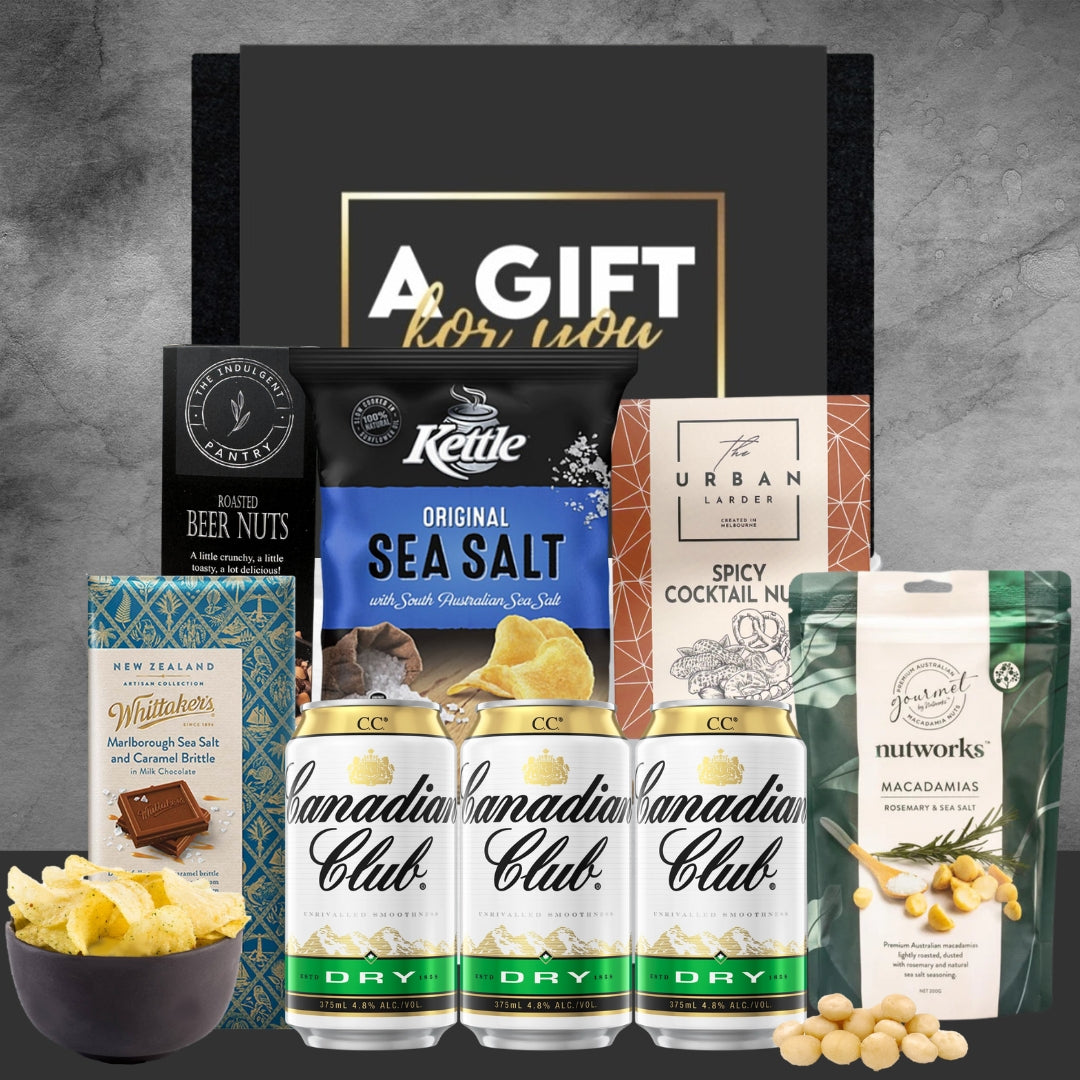 Gift set with Canadian Club whisky, Kettle chips, and other snacks on a gray background