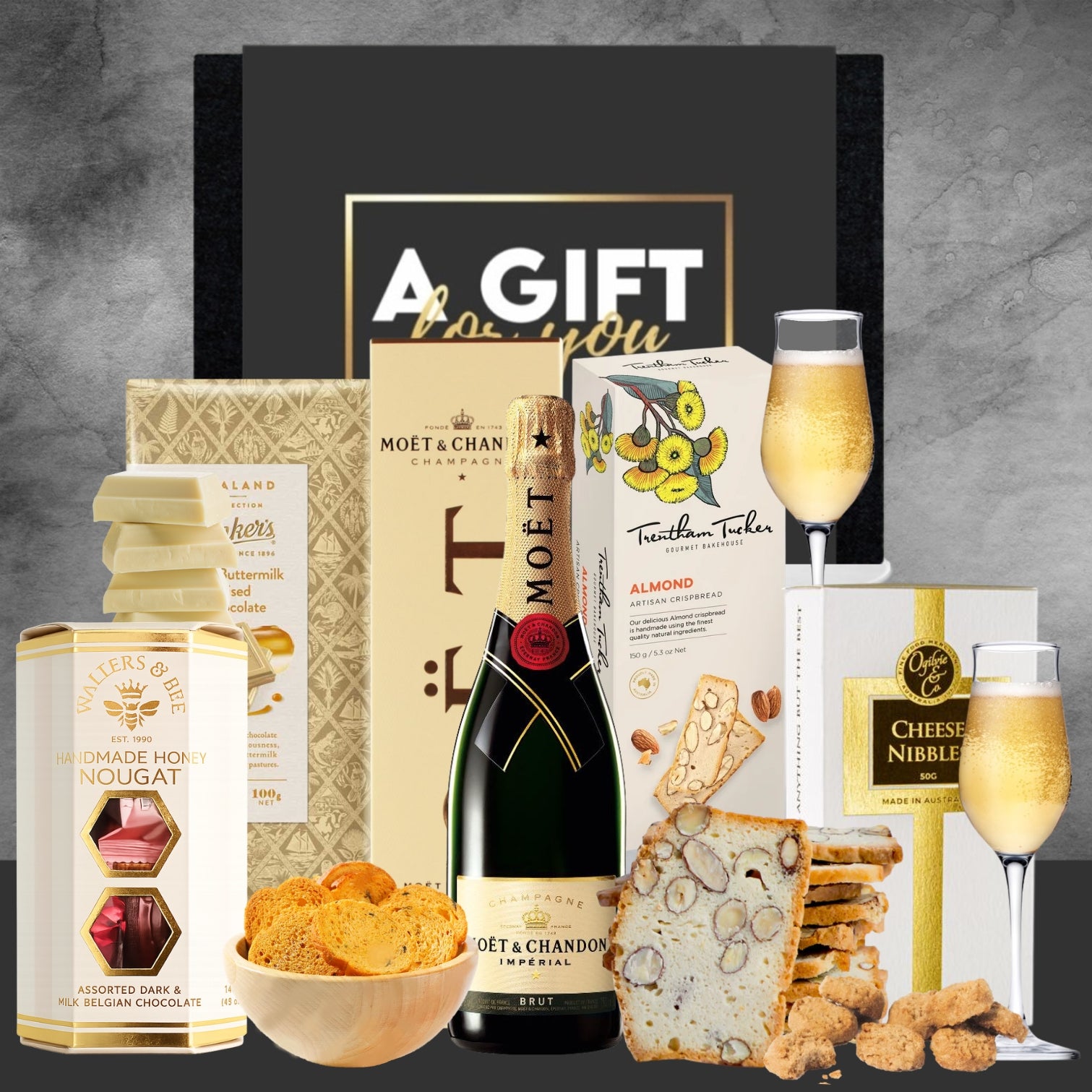 Gift set with Moët & Chandon champagne, chocolates, and snacks on a gray background.