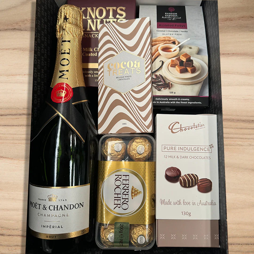 Gift set with Moët & Chandon champagne, Ferrero Rocher chocolates, and chocolate bars on a wooden surface.