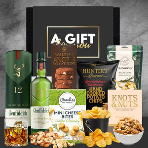 Gift set with Glenfiddich whiskey, snacks, and a 'A Gift for You' card on a gray background.