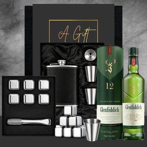 Glenfiddich 12 whisky bottle with cocktail shaker set, ice cubes, and shot glasses on a gray background.