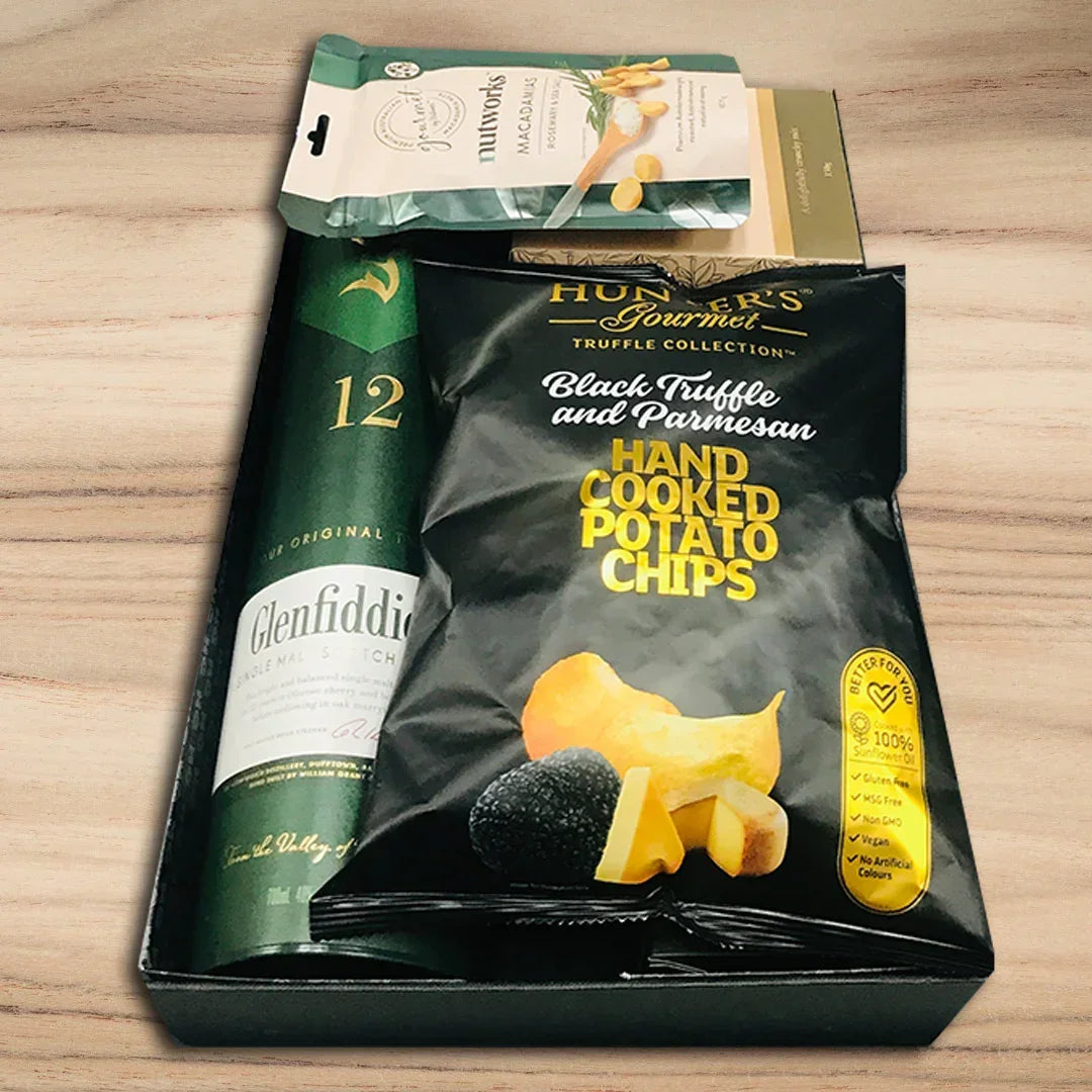 Packaging of Glenfiddich whisky and Hunter's Gourmet black truffle and Parmesan potato chips on a wooden surface.