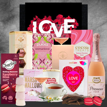 Gourmet gift basket with chocolate, tea, and a bottle of Prosecco on a gray background