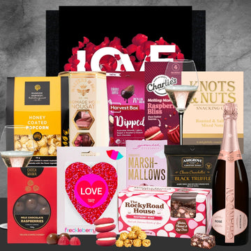 Gourmet gift basket with chocolate, popcorn, and a bottle of champagne on a gray background.