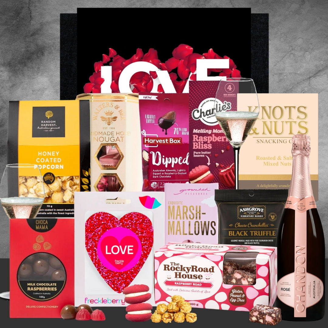Gourmet gift basket with chocolate, popcorn, and a bottle of champagne on a gray background.