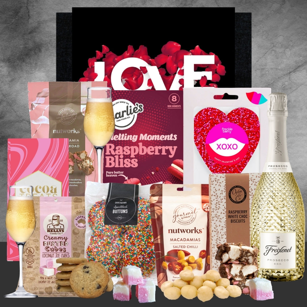 Gourmet gift basket with snacks, drinks, and a 'LOVE' magazine on a gray background