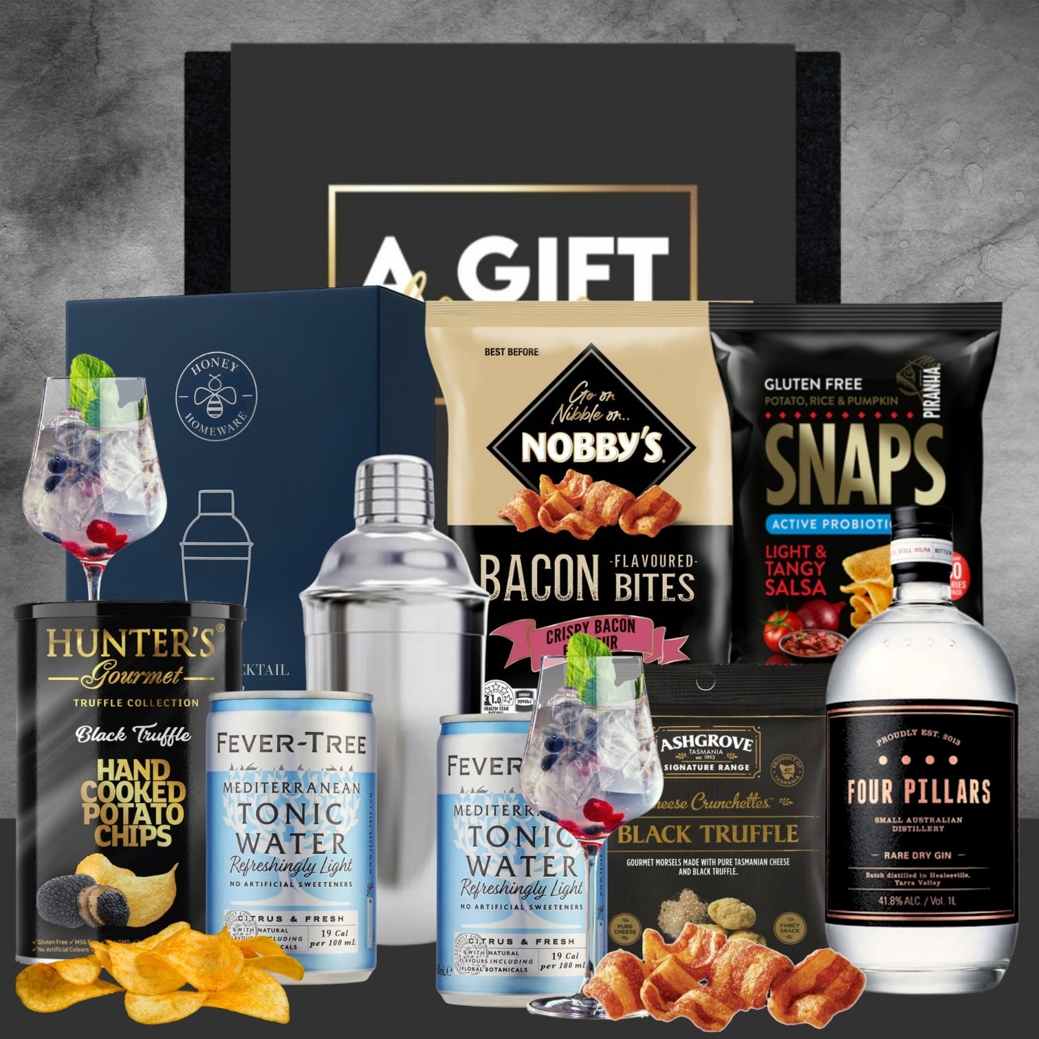 Gourmet gift set with drinks, snacks, and a cocktail shaker on a gray background.