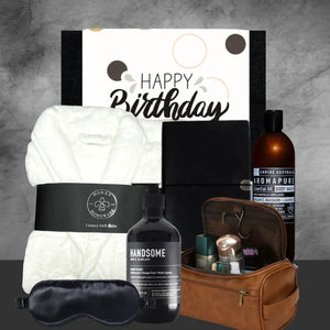 Grooming and relaxation gift set with bath products, towel, and sleep mask on a gray background.