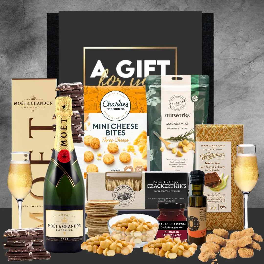 Gourmet gift basket with champagne, snacks, and chocolate on a gray background