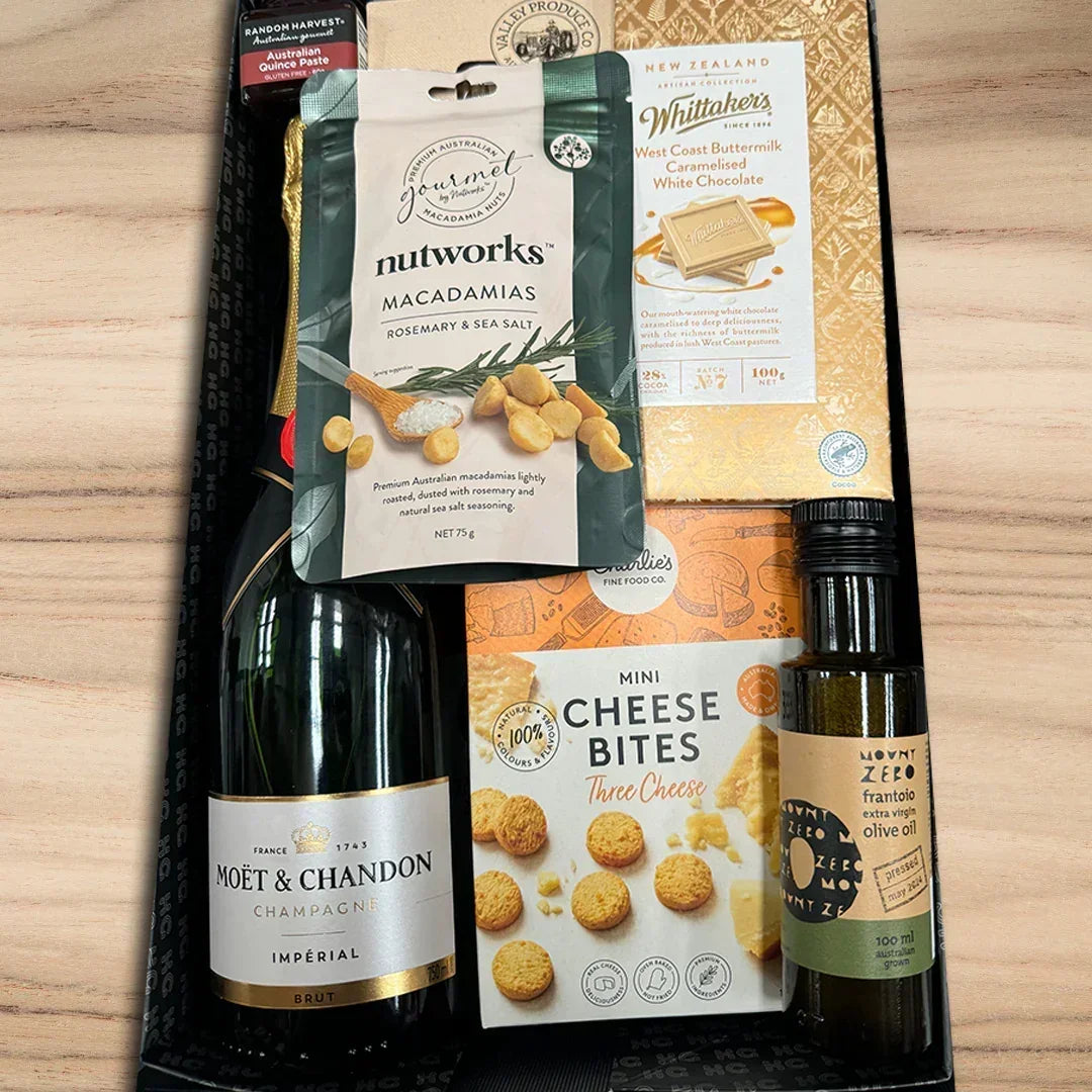 Gift set with Moët & Chandon champagne, nutworks macadamias, Whittaker's chocolate, and olive oil on a wooden surface.