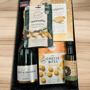 Gift set with Moët & Chandon champagne, nutworks macadamias, Whittaker's chocolate, and olive oil on a wooden surface.