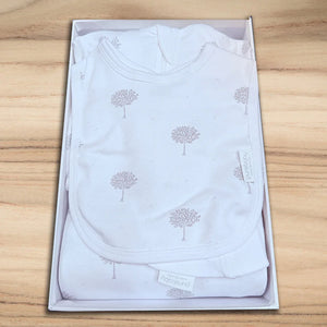 White baby onesie with tree pattern in a box on a wooden surface